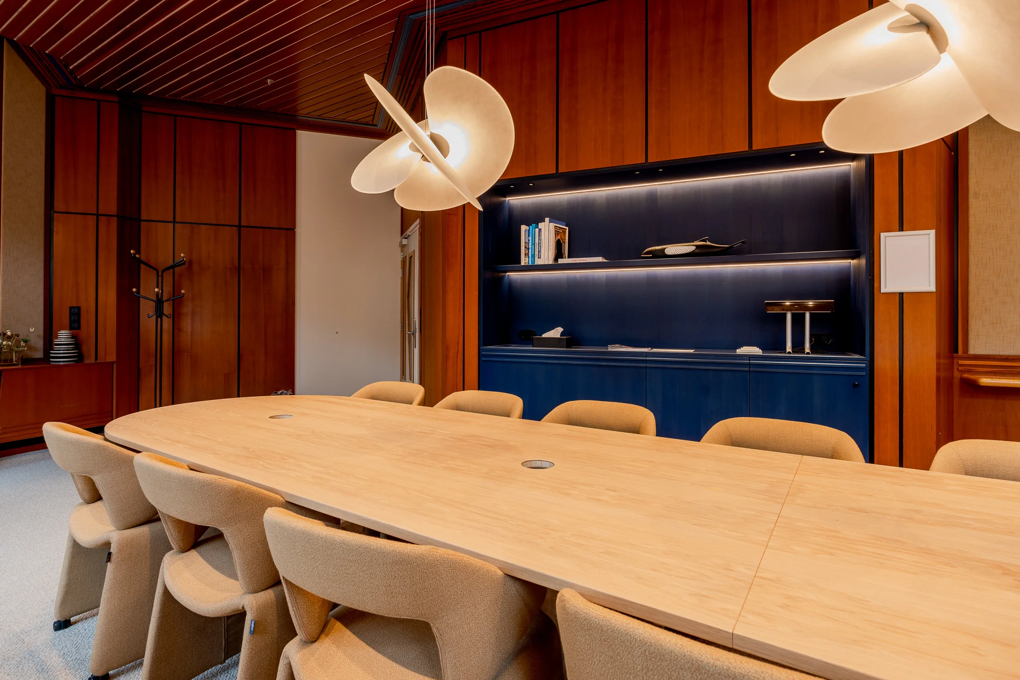 Vergaderruimte met lange houten tafel, beige stoelen, moderne verlichting en donkere houten wandkasten in het Zandkasteel.