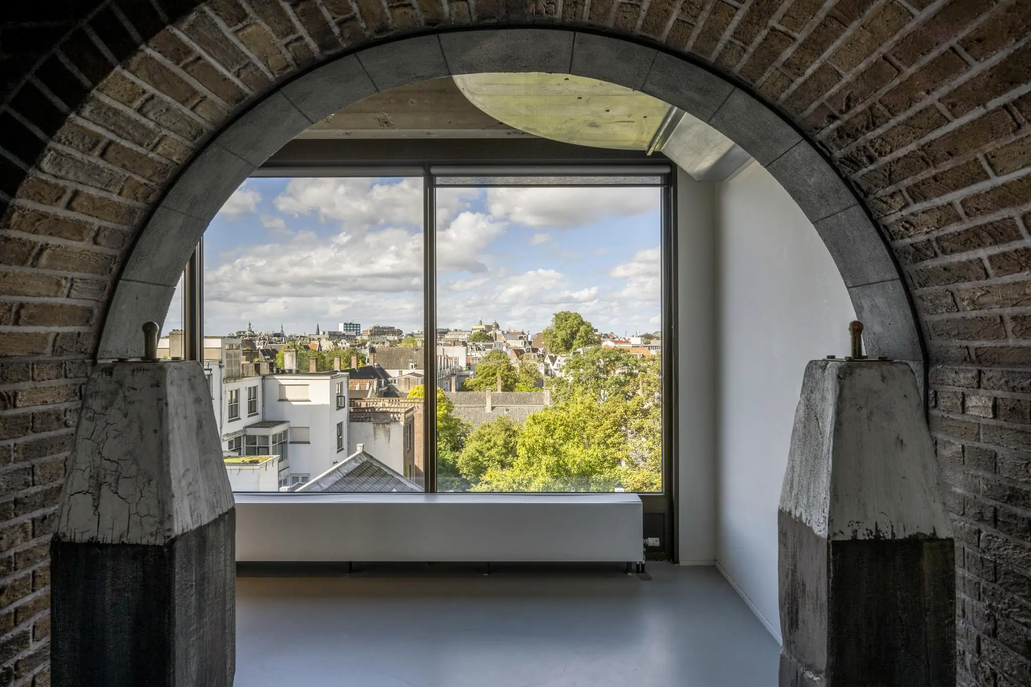 Uitzicht op de Amsterdamse Vijzelstraat door een grote boograam in een modern gerenoveerde ruimte met bakstenen muur.
