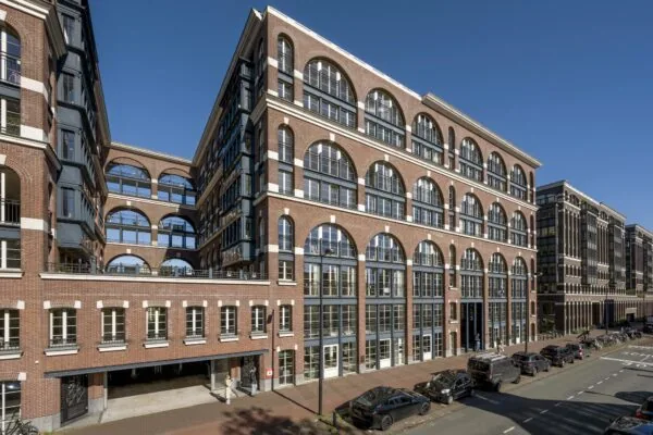 Modern woongebouw aan de Oostelijke Handelskade in Amsterdam met opvallende bakstenen gevel en grote boogramen.