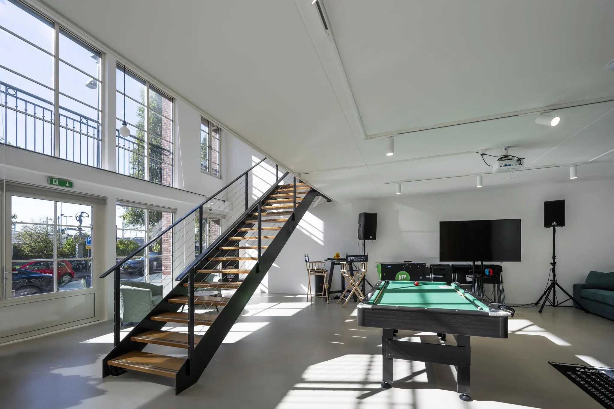 Moderne, lichtovergoten recreatieruimte aan de Oostelijke Handelskade met een pooltafel, trap en grote ramen.