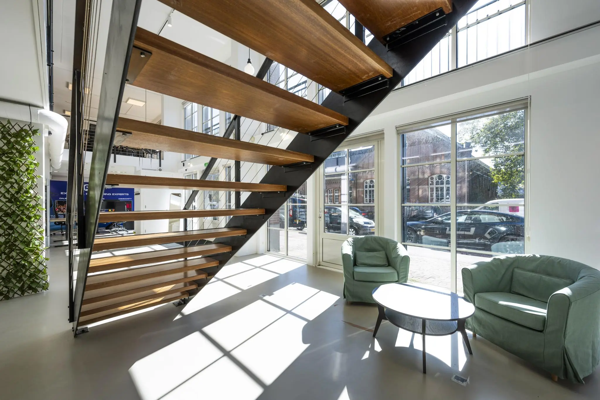 Moderne kantoorruimte aan de Oostelijke Handelskade met een houten open trap, grote ramen en een zithoek met twee groene fauteuils.