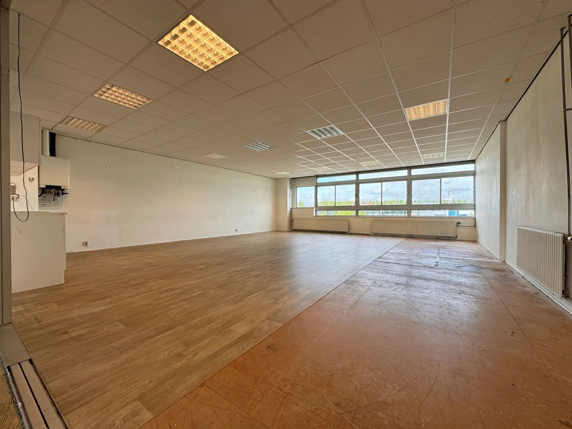 Leeg kantoor- of bedrijfsruimte aan de Hoofdweg met grote ramen en systeemplafond.