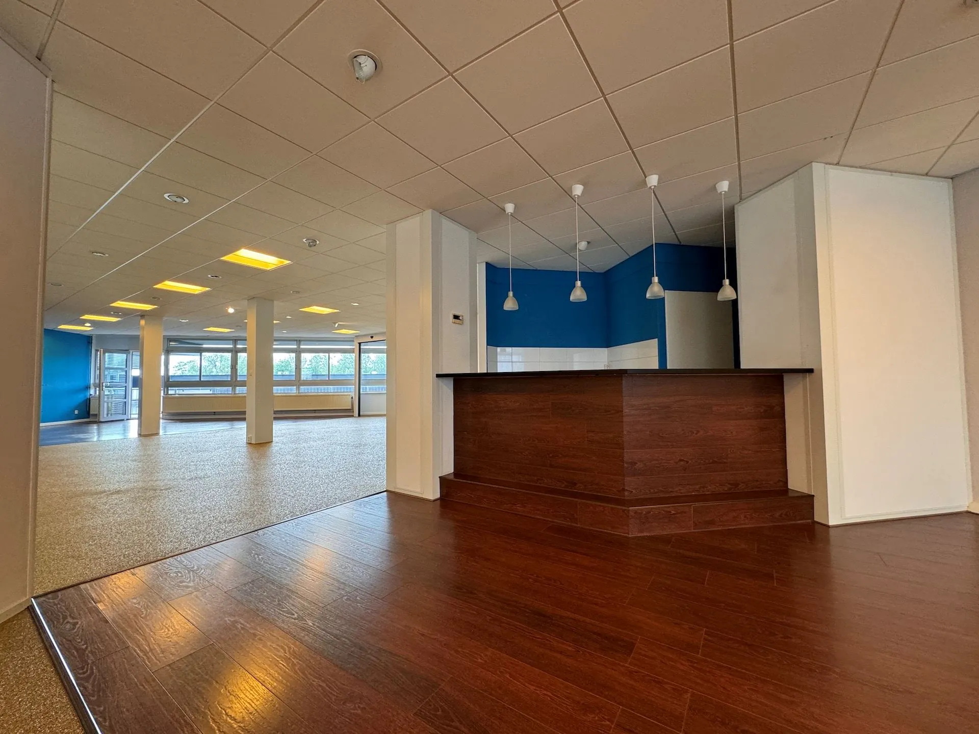 Moderne, open ruimte in een bedrijfs- of kantoorpand aan de Hoofdweg met houten vloer en een balie met hanglampen.