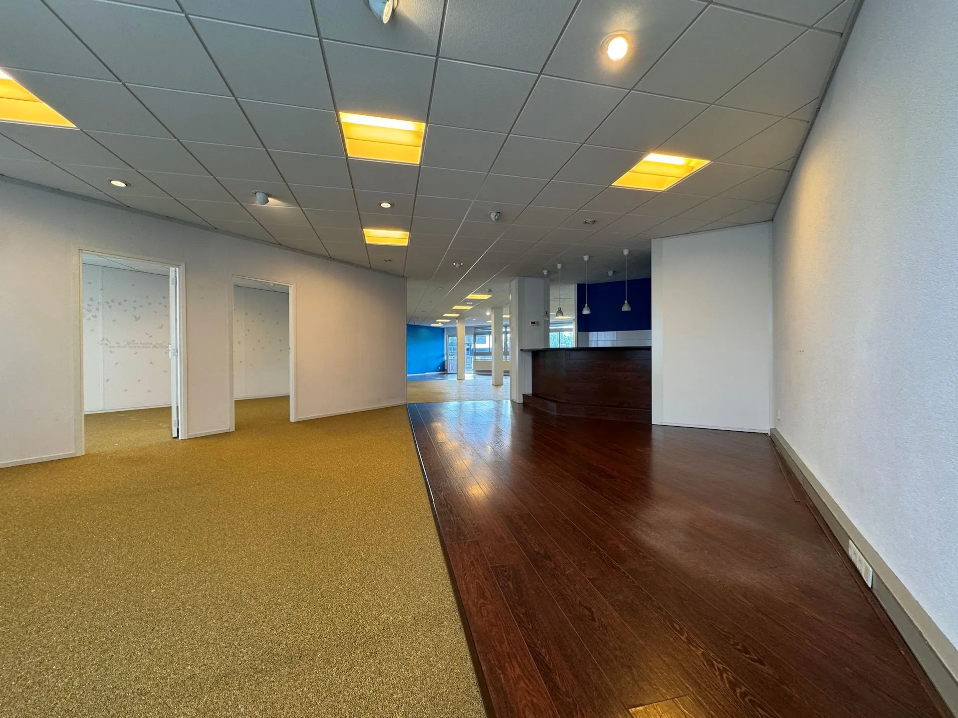 Kantoorruimte aan de Hoofdweg met houten vloer, tapijt, meerdere kantoorruimtes en een balie.