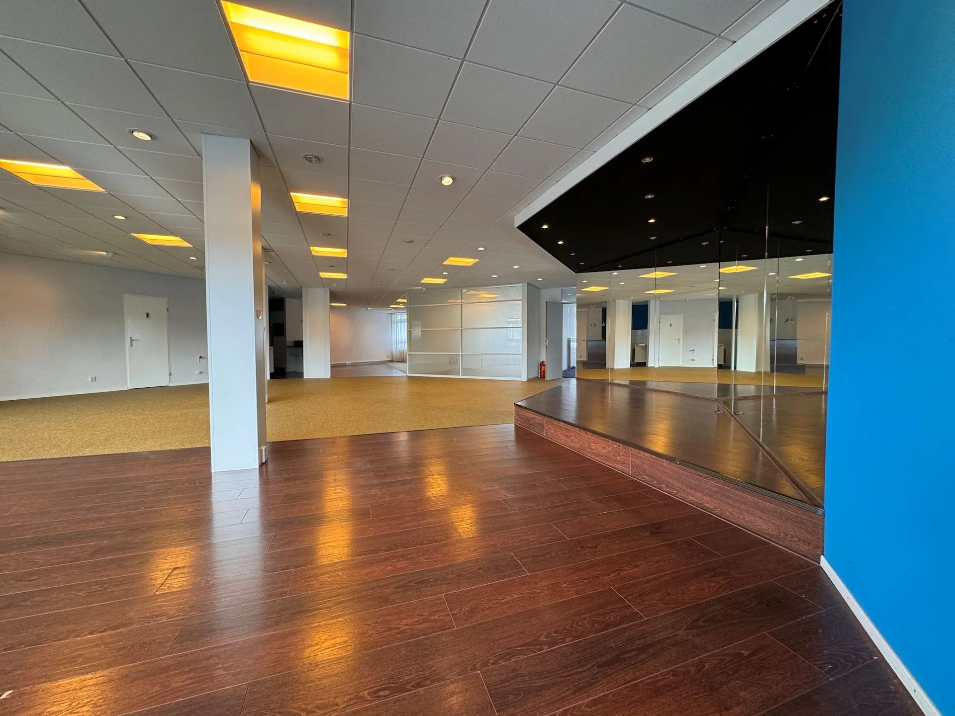 Leeg bedrijfsruimte-interieur aan de Hoofdweg met houten vloer, spiegelwand en systeemplafondverlichting.