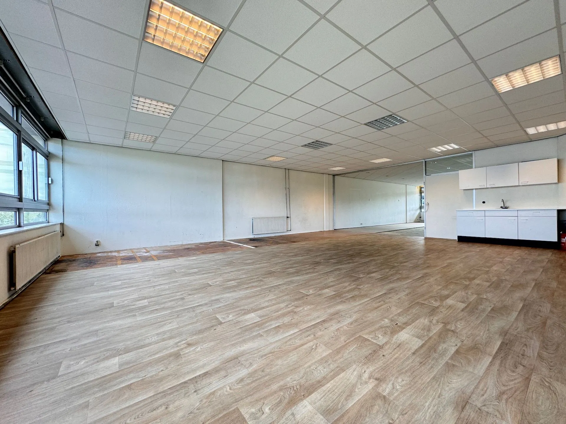 Lege kantoorruimte aan de Hoofdweg met houten vloer, systeemplafond, keukenblok en grote ramen.