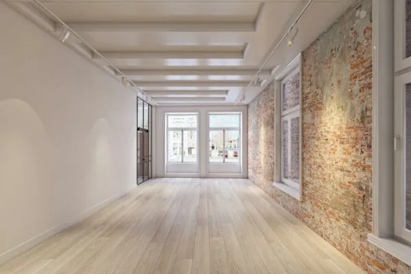 Licht en modern appartement aan het Rokin met houten vloer, grote ramen en een karakteristieke bakstenen muur.