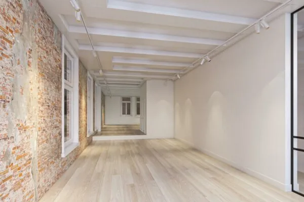Licht, leeg interieur aan het Rokin met houten vloer, bakstenen muur en witte balkenplafonds.