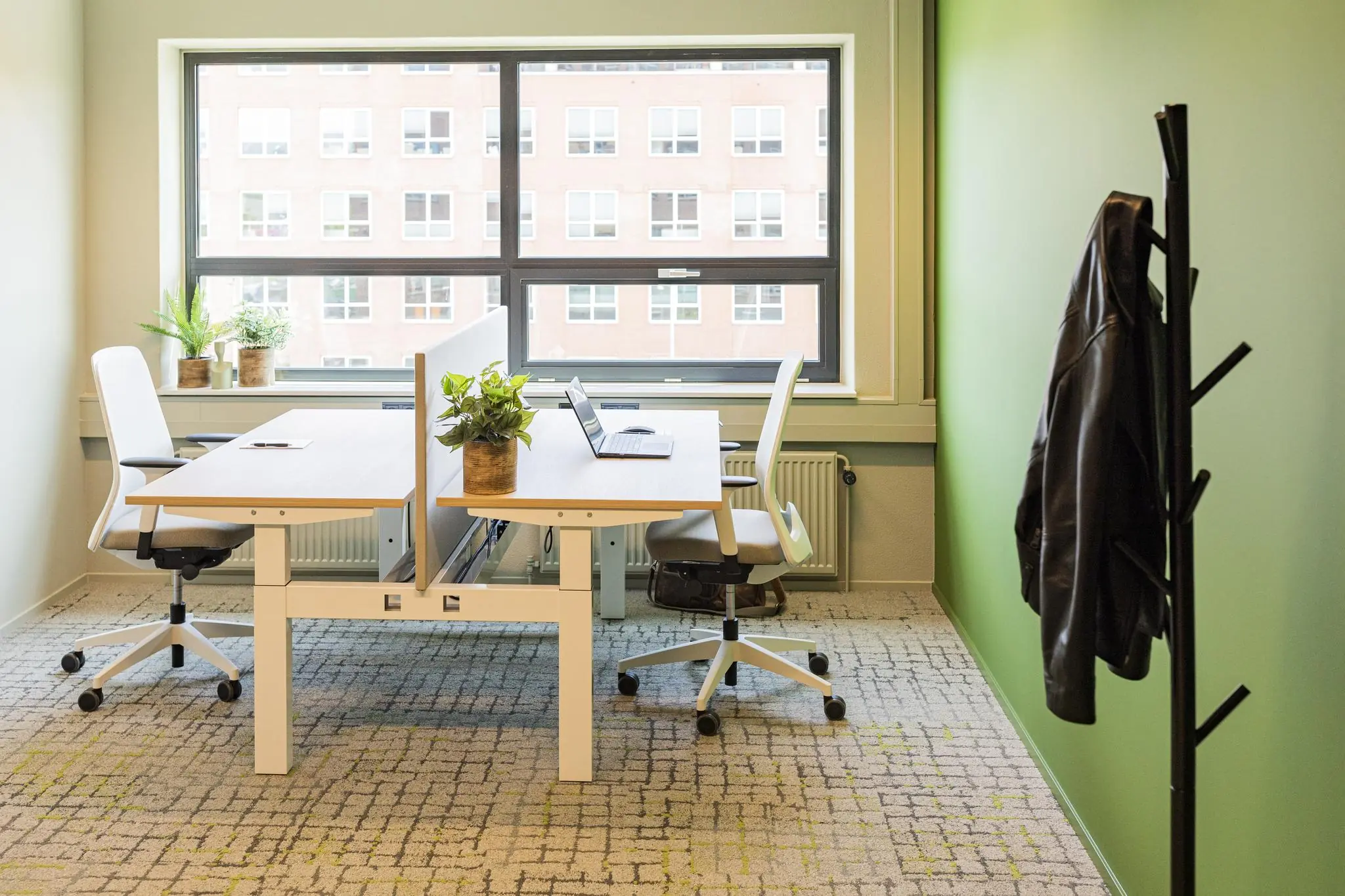 Moderne, lichte kantoorruimte in Rijnzathe met twee werkplekken, laptops, planten en een jas aan de kapstok.
