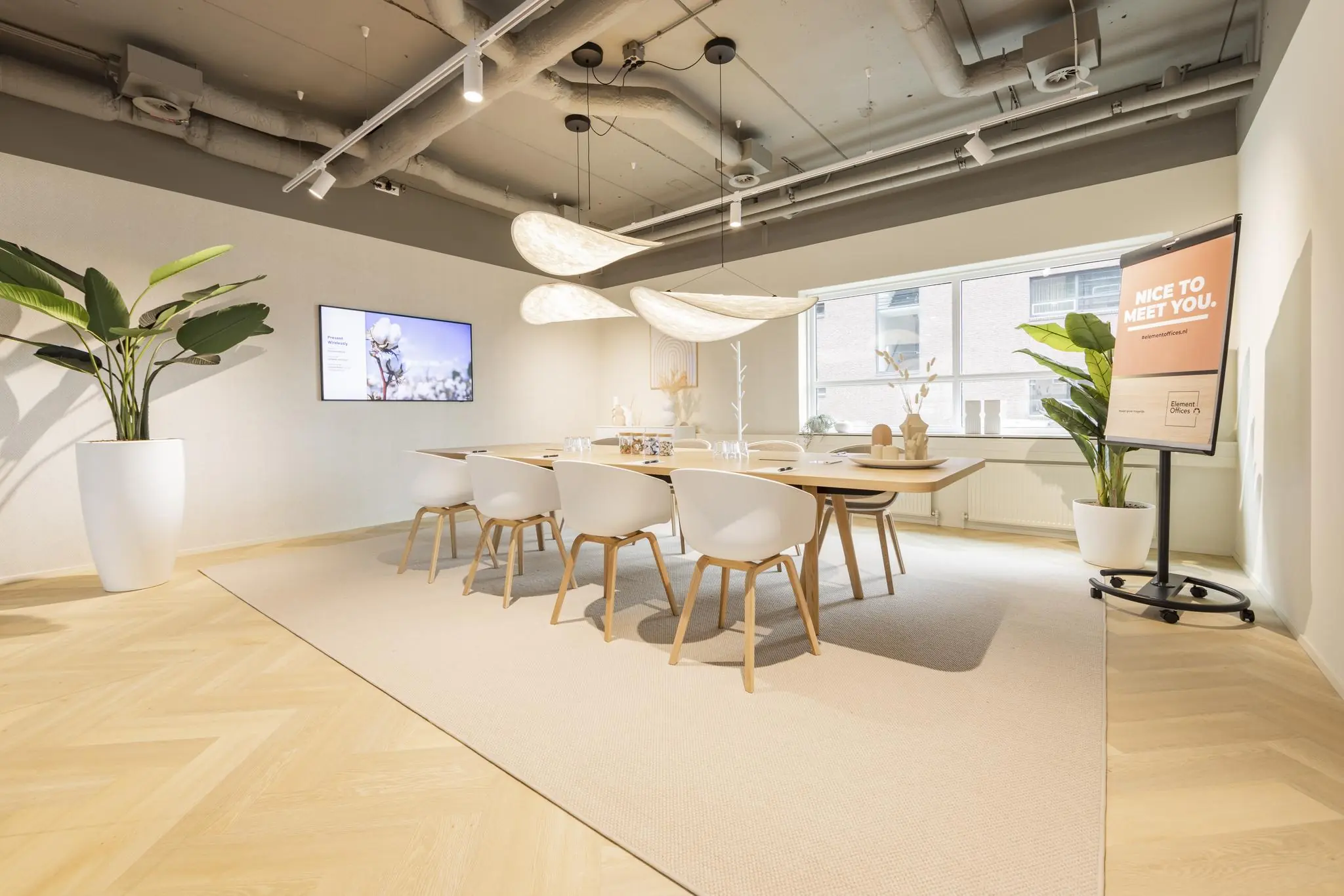 Stijlvolle en moderne vergaderruimte in Rijnzathe met houten tafel, witte stoelen, grote planten en zachte verlichting.