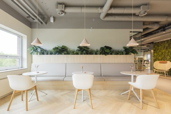 Moderne en lichte zithoek in kantoorgebouw Rijnzathe, met witte stoelen, ronde tafels, hanglampen en een groene plantenwand.
