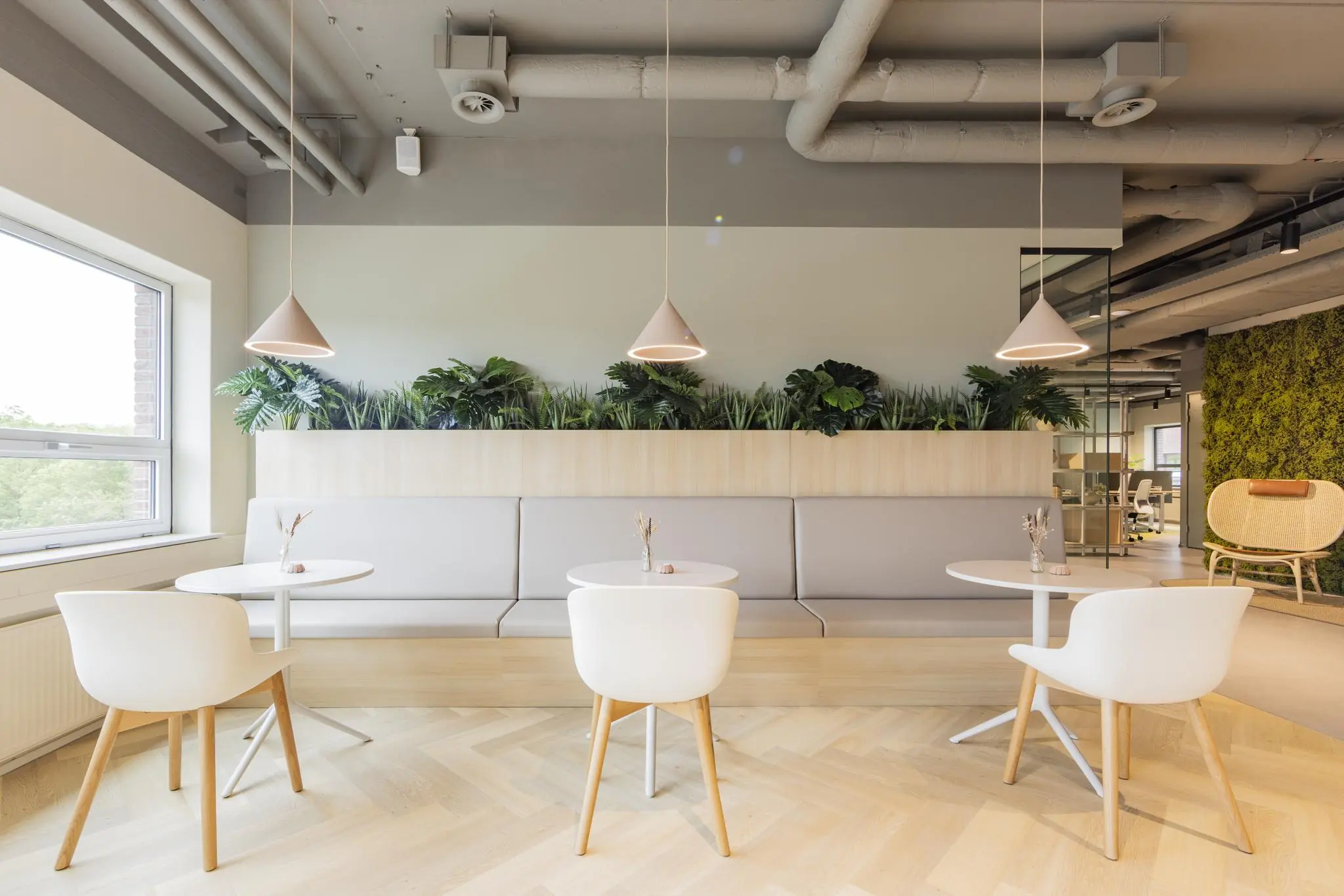 Moderne en lichte zithoek in kantoorgebouw Rijnzathe, met witte stoelen, ronde tafels, hanglampen en een groene plantenwand.