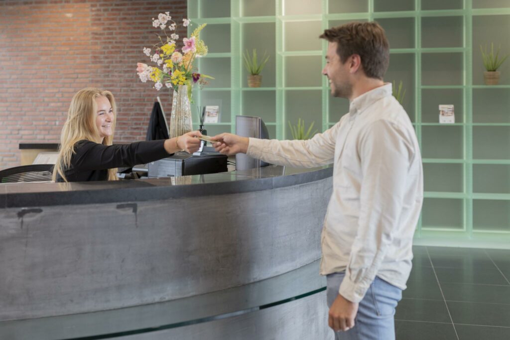 Man overhandigt een pas bij de receptie van een modern gebouw aan de Rijnzathe.