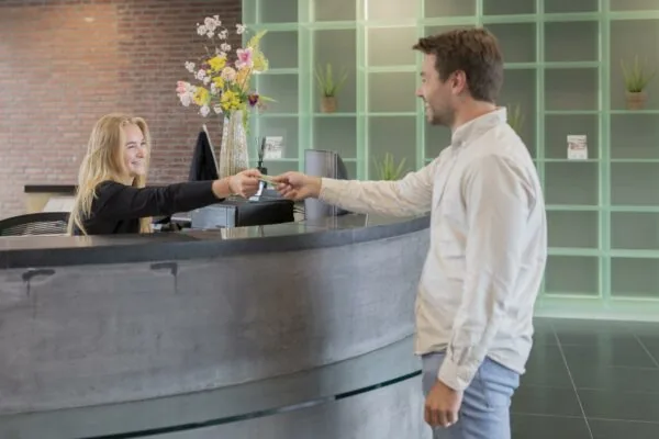 Man overhandigt een pas bij de receptie van een modern gebouw aan de Rijnzathe.