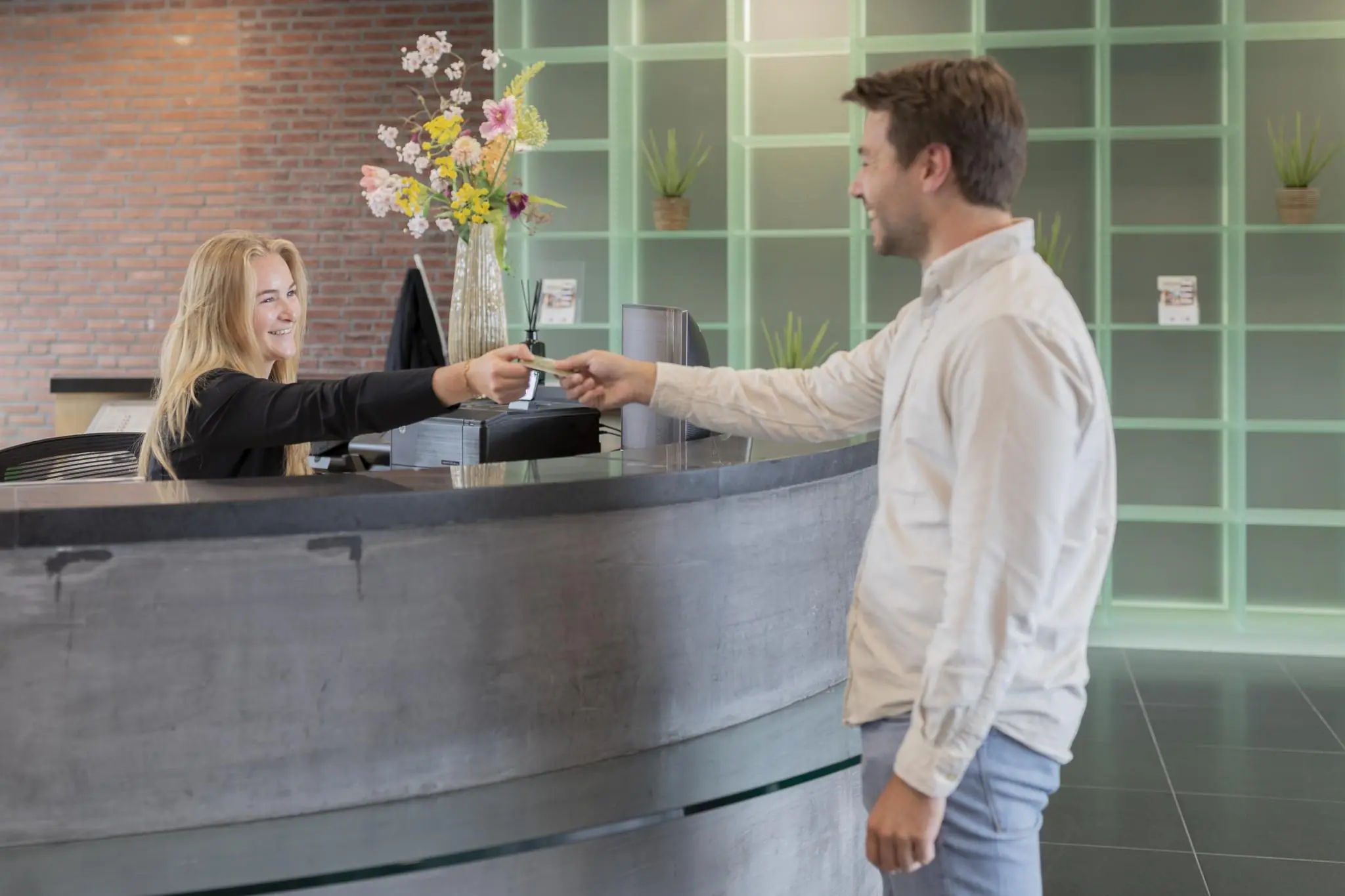 Man overhandigt een pas bij de receptie van een modern gebouw aan de Rijnzathe.