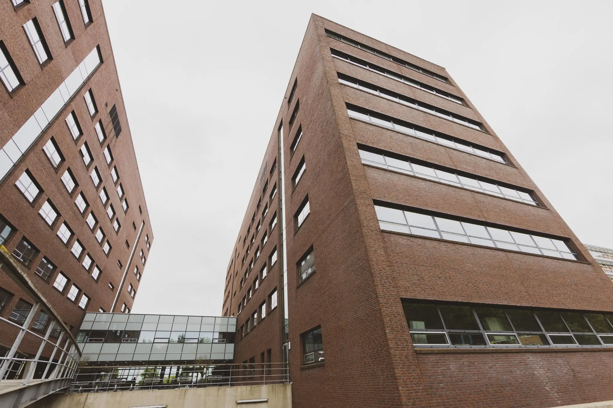 Twee roodbruine kantoorgebouwen aan de Rijnzathe, verbonden door een glazen loopbrug.