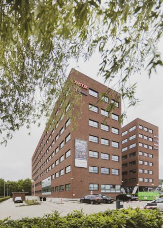 Kantoorgebouw Rijnzathe met onder meer de logo’s van Xerox, Hageman en Proact, gefotografeerd vanaf de parkeerplaats met bomen op de voorgrond.