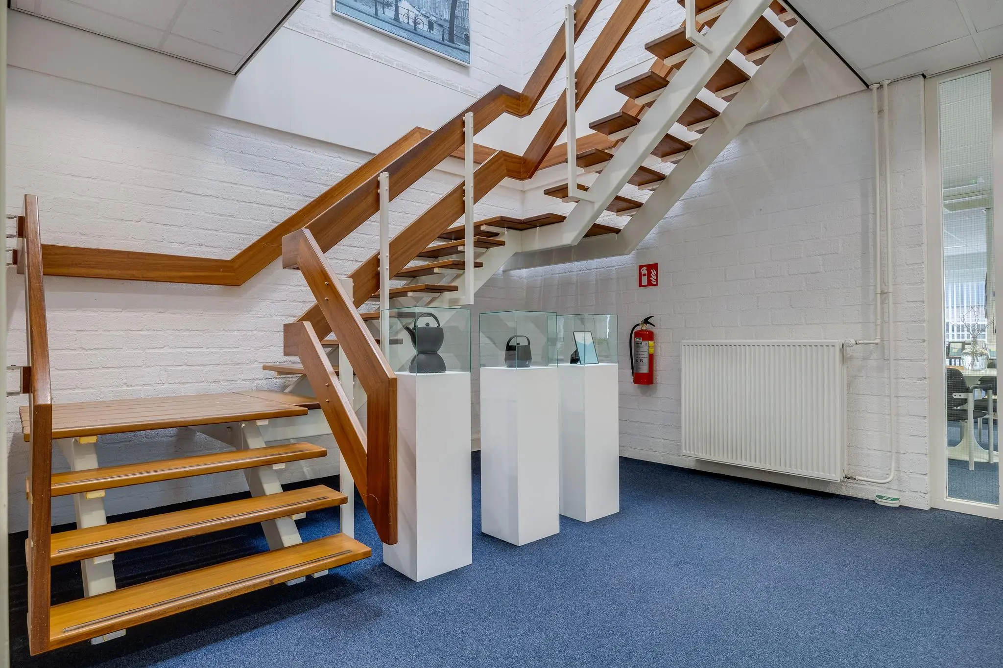 Moderne houten trap in een kantoorruimte aan de Savannahweg met drie vitrinekasten en blauwe vloerbedekking.