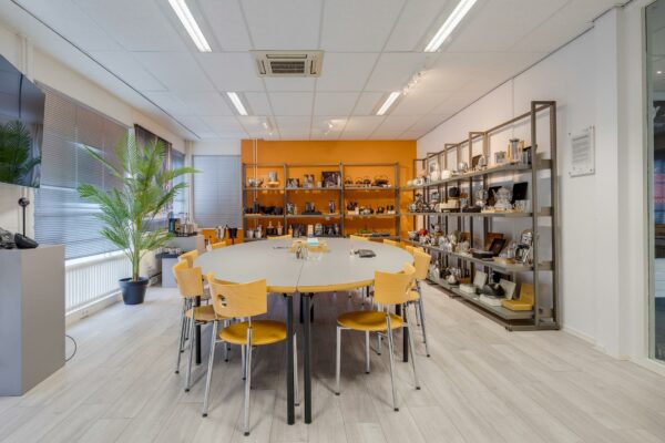 Vergaderruimte aan de Savannahweg met ovale tafel, houten stoelen en stalen stellingen vol met koffie- en theekannen.
