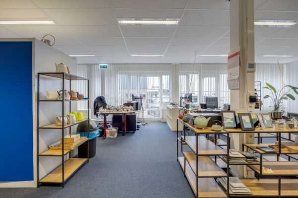 Modern kantoor aan de Savannahweg met open werkplekken, stellingen vol theepotten en fotolijsten, en veel daglicht door grote ramen.