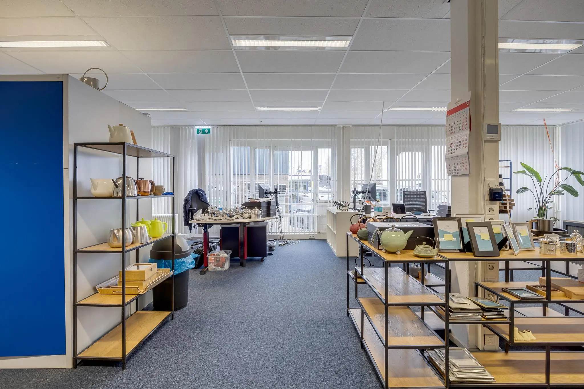 Modern kantoor aan de Savannahweg met open werkplekken, stellingen vol theepotten en fotolijsten, en veel daglicht door grote ramen.