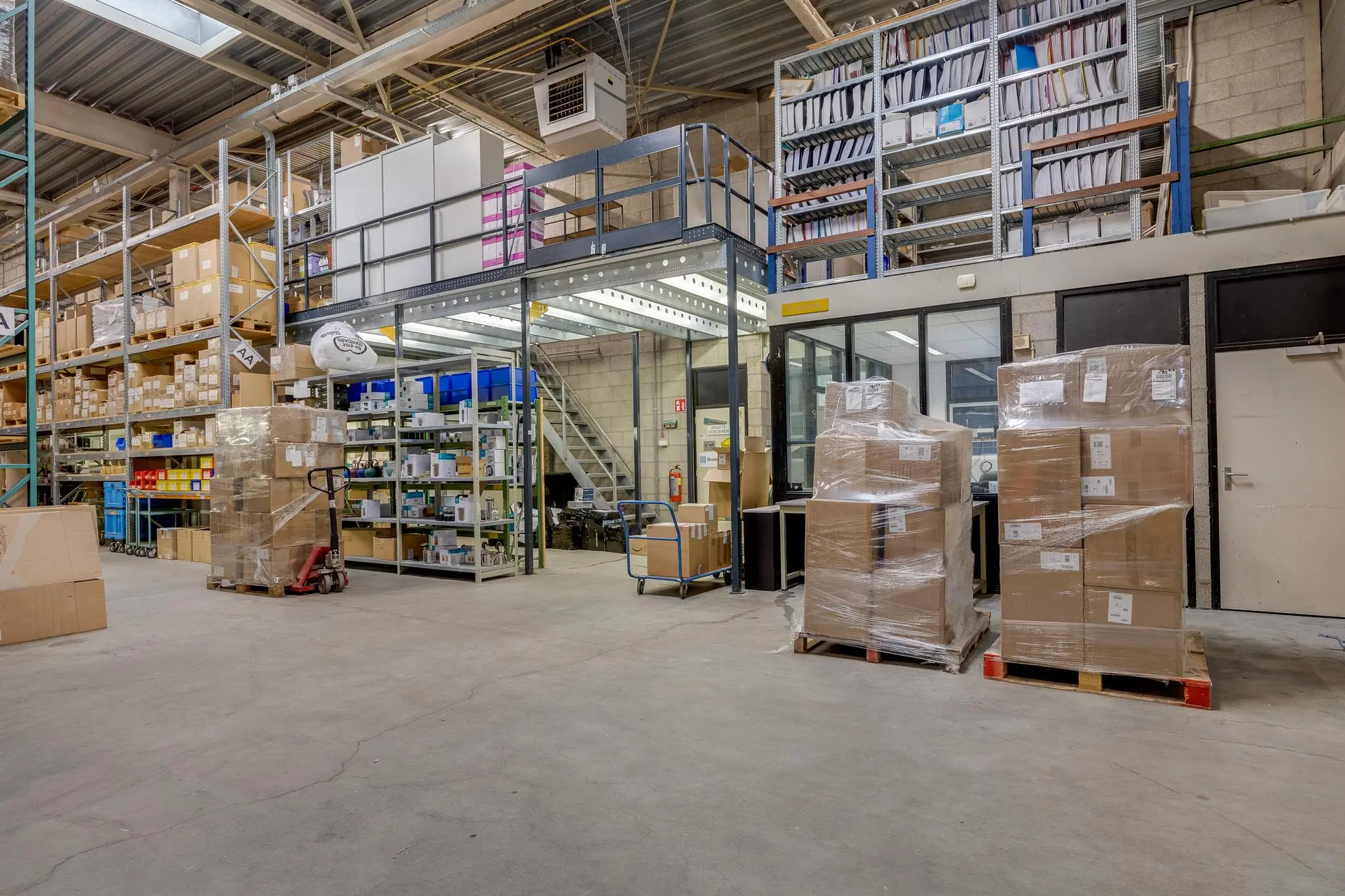 Magazijn aan de Savannahweg met stellingen vol dozen, pallets met verpakte goederen en een kantoorruimte op de achtergrond.