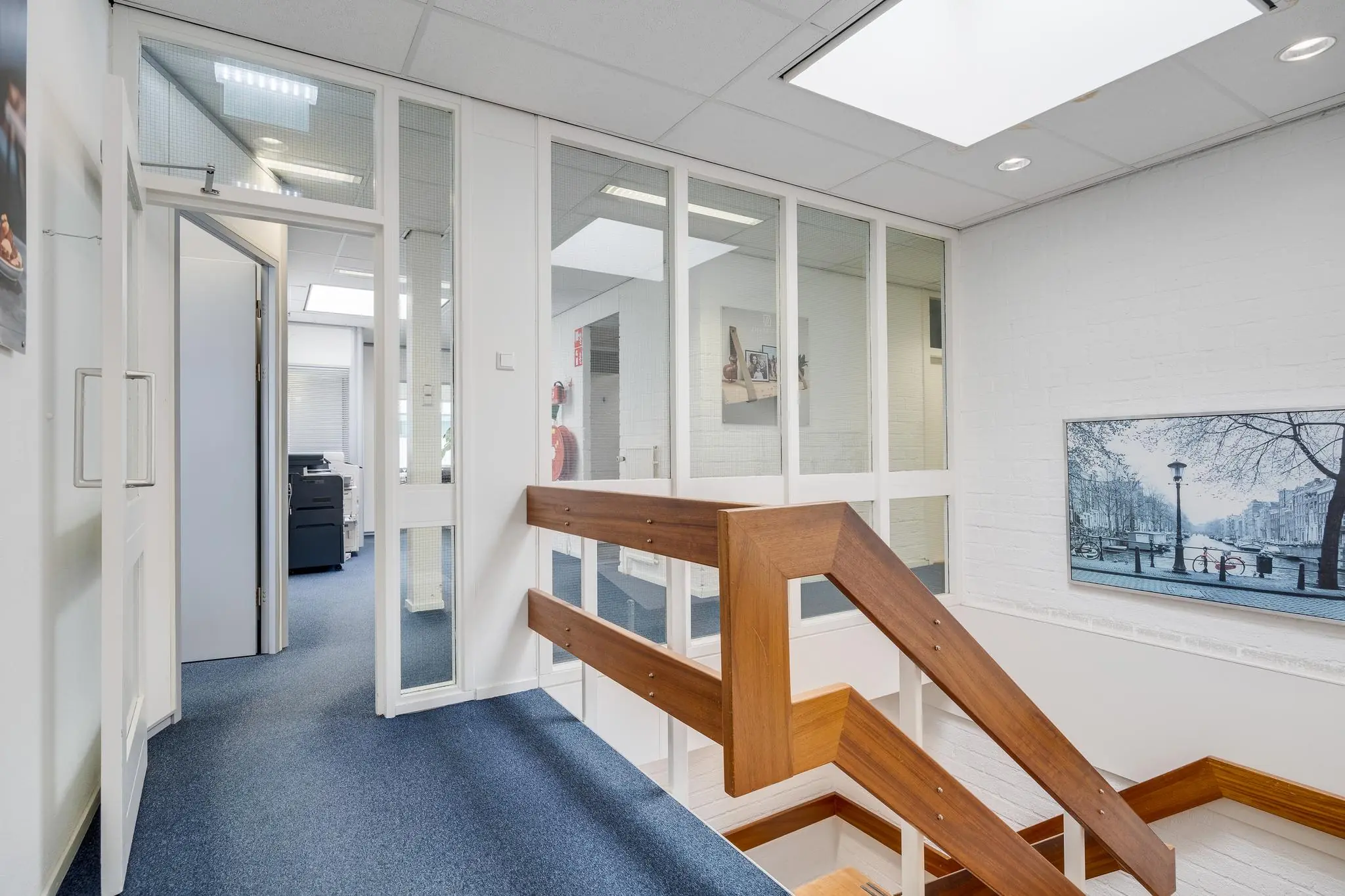 Trapopgang met houten leuning in een modern kantoorpand aan de Savannahweg, met blauwe vloerbedekking en glazen kantoormuren.