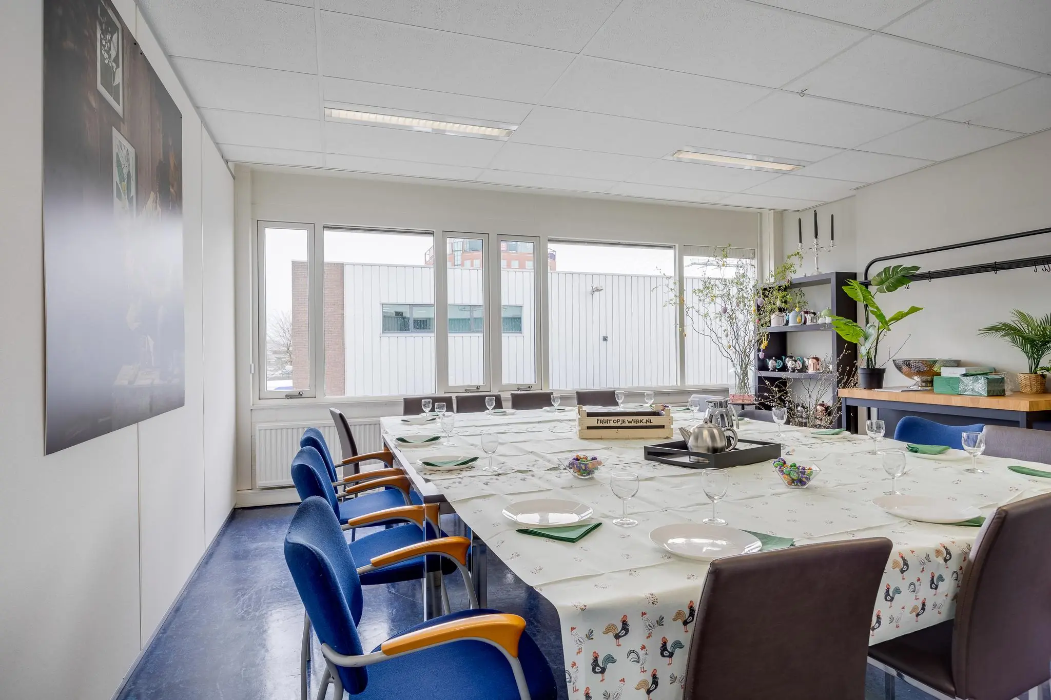 Vergaderruimte aan de Savannahweg met een gedekte tafel, omringd door stoelen en ingericht met planten en servies.