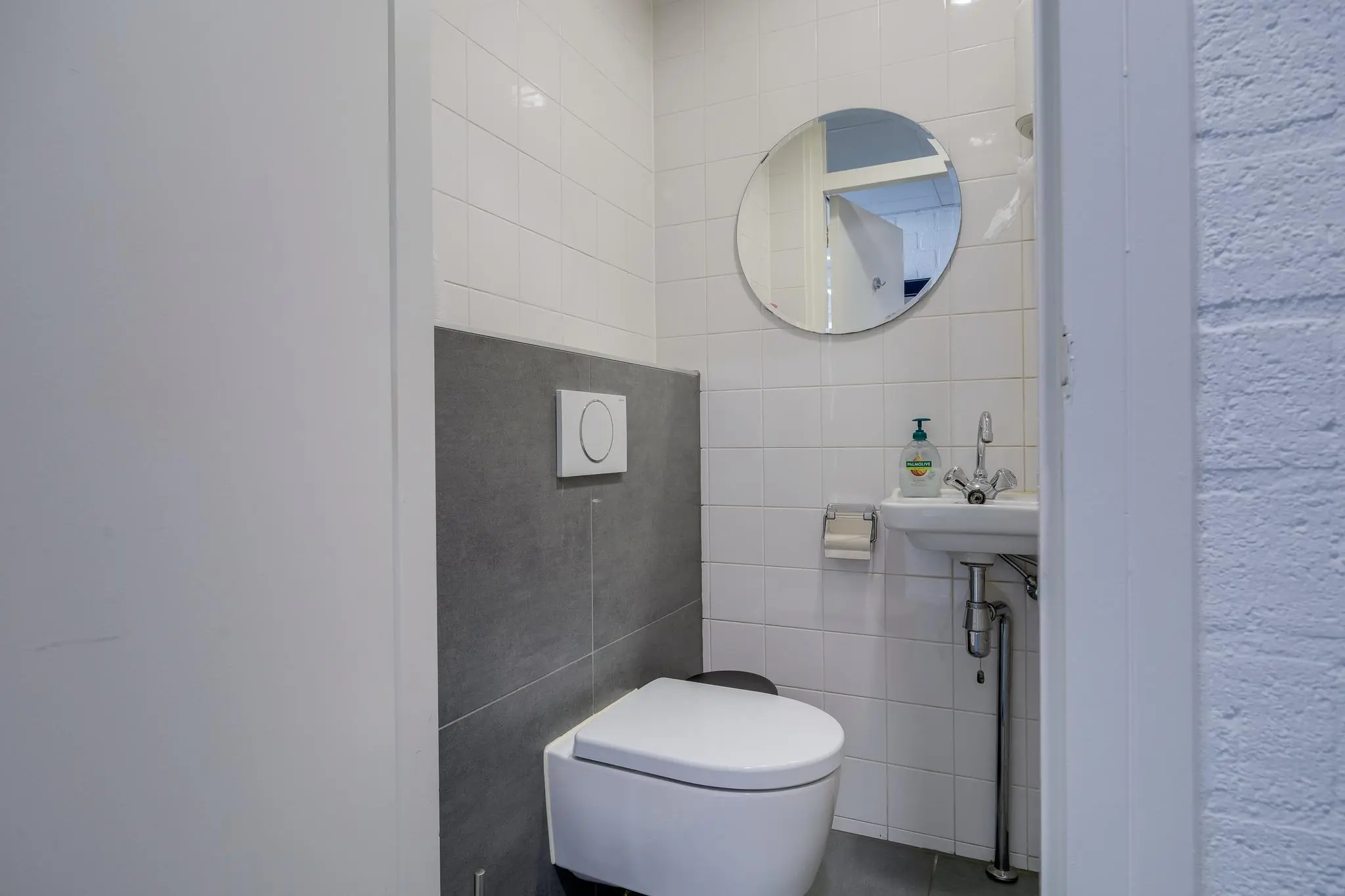 Moderne toiletruimte met hangtoilet, fontein, ronde spiegel en witte wandtegels aan de Savannahweg.