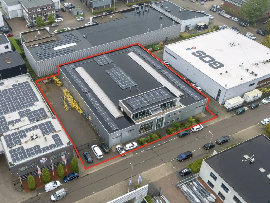 Luchtfoto van een bedrijfsgebouw aan de Tennesseedreef met zonnepanelen op het dak, rood omlijnd om het perceel aan te duiden.