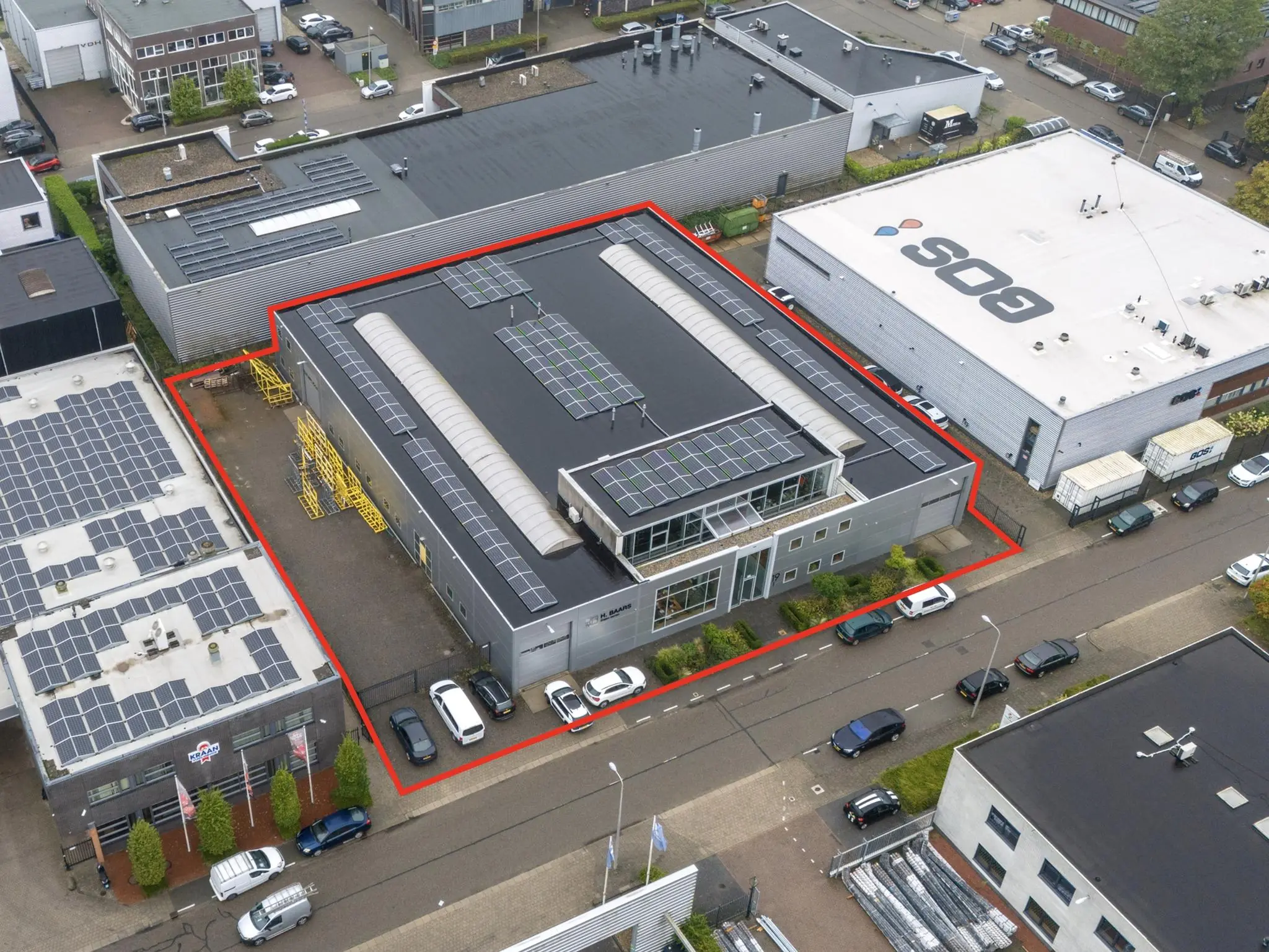 Luchtfoto van een bedrijfsgebouw aan de Tennesseedreef met zonnepanelen op het dak, rood omlijnd om het perceel aan te duiden.
