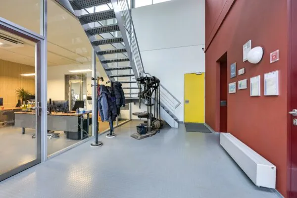 Ingang en trappenhuis van een modern kantoorpand aan de Tennesseedreef met zicht op kantoorruimte en gele deur.