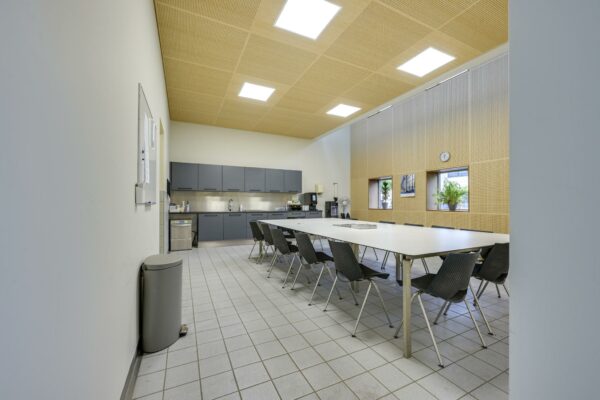 Moderne kantineruimte aan de Tennesseedreef met lange vergadertafel, keukenblok en grote ramen met planten.