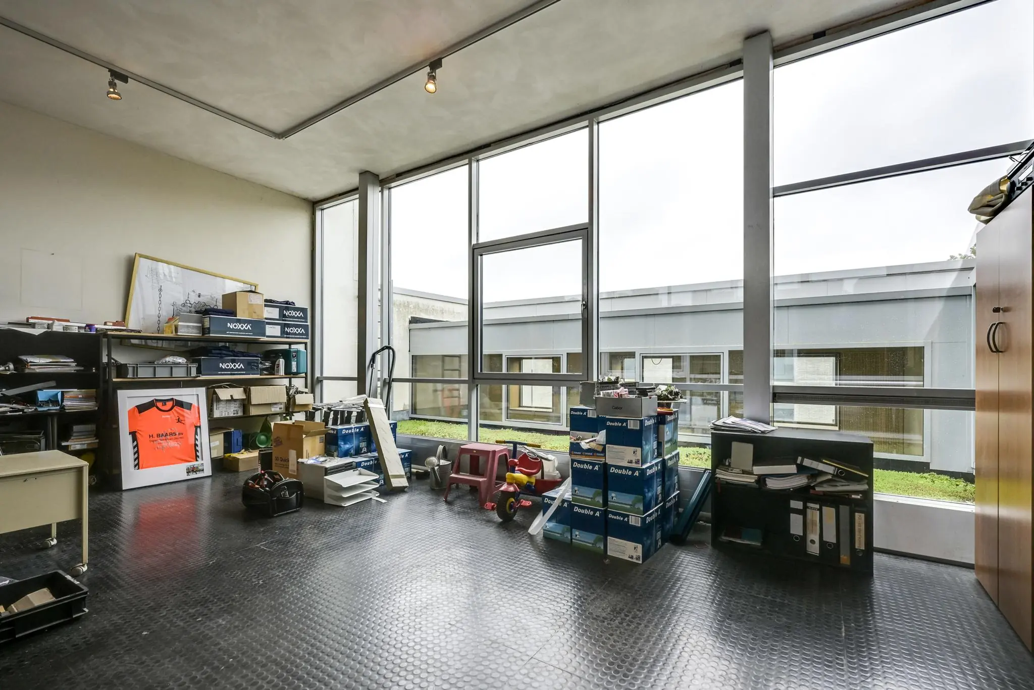 Kantoorruimte aan de Tennesseedreef met grote ramen en opslag van kantoormaterialen en dozen.