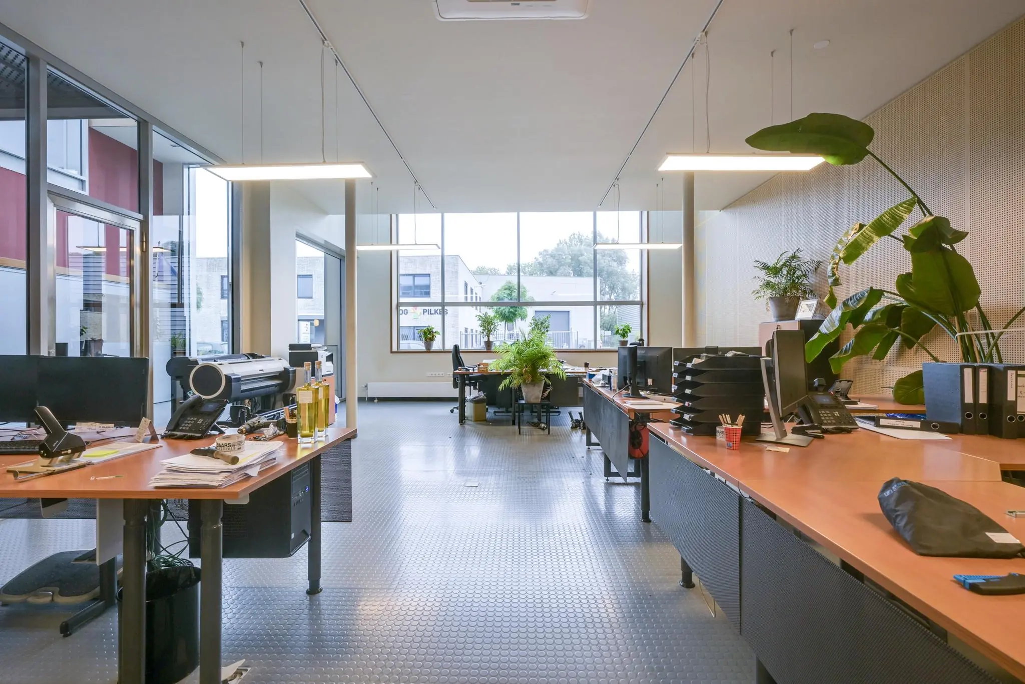 Modern kantoorinterieur aan de Tennesseedreef met grote ramen, bureaus, planten en apparatuur.