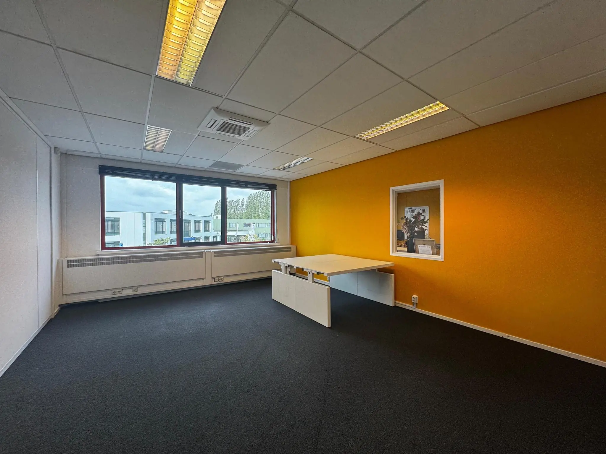 Kantoorruimte aan de Kwekerijweg met gele accentmuur, groot raam en een wit bureau.