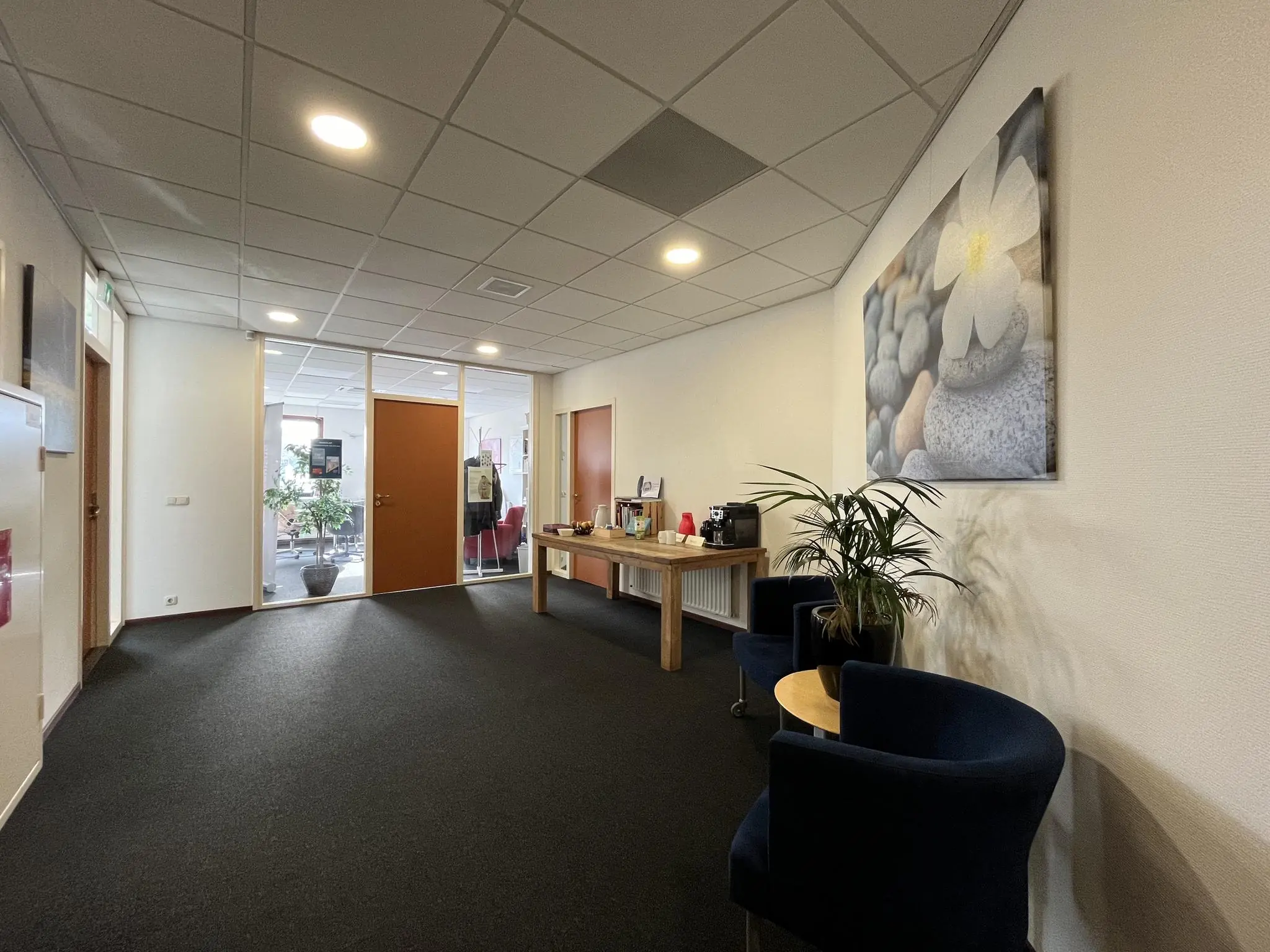 Wachtruimte in een kantoor aan de Kwekerijweg met koffiehoek, zitgelegenheid en een grote fotoprint van een bloem aan de muur.