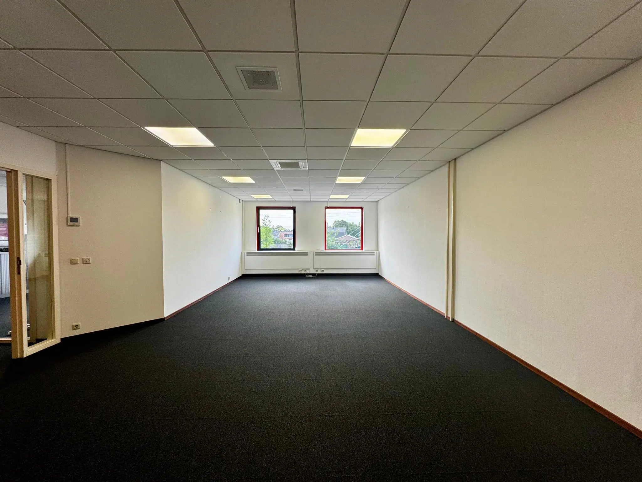 Leeg kantoorpand aan de Kwekerijweg met systeemplafond, zwart tapijt en twee ramen aan de achterzijde.