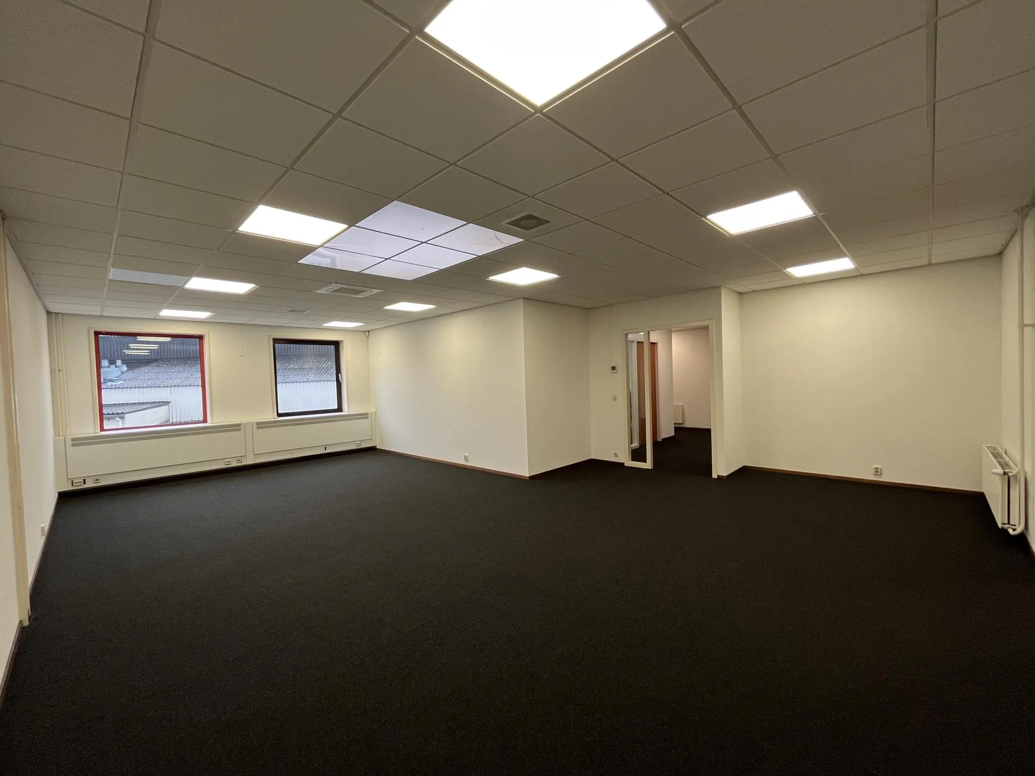 Leeg kantoorruimte met systeemplafond, zwarte vloerbedekking en twee ramen aan de Kwekerijweg.