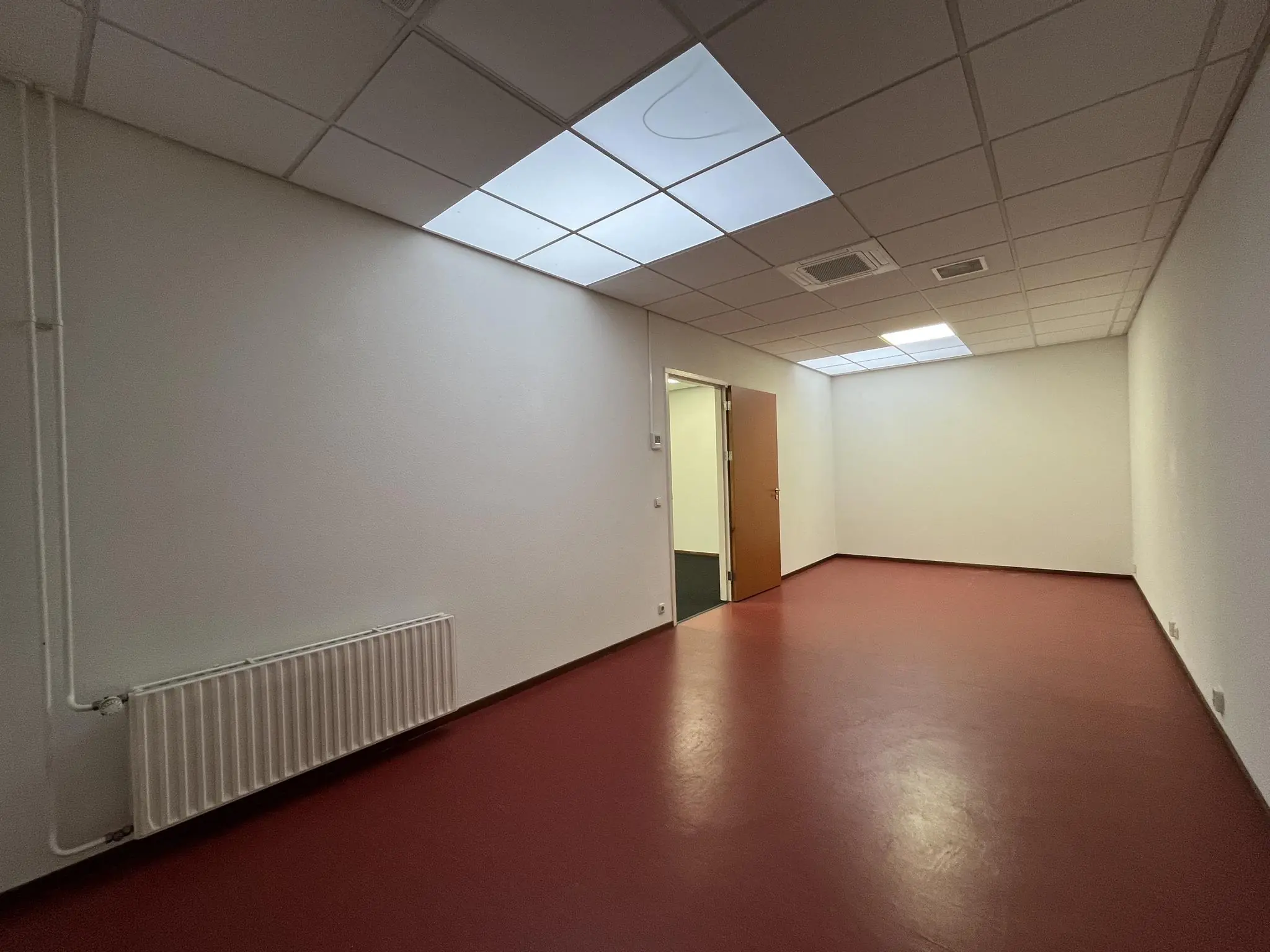 Lege kantoorruimte aan de Kwekerijweg met rode vloer, witte muren en systeemplafond met verlichting.