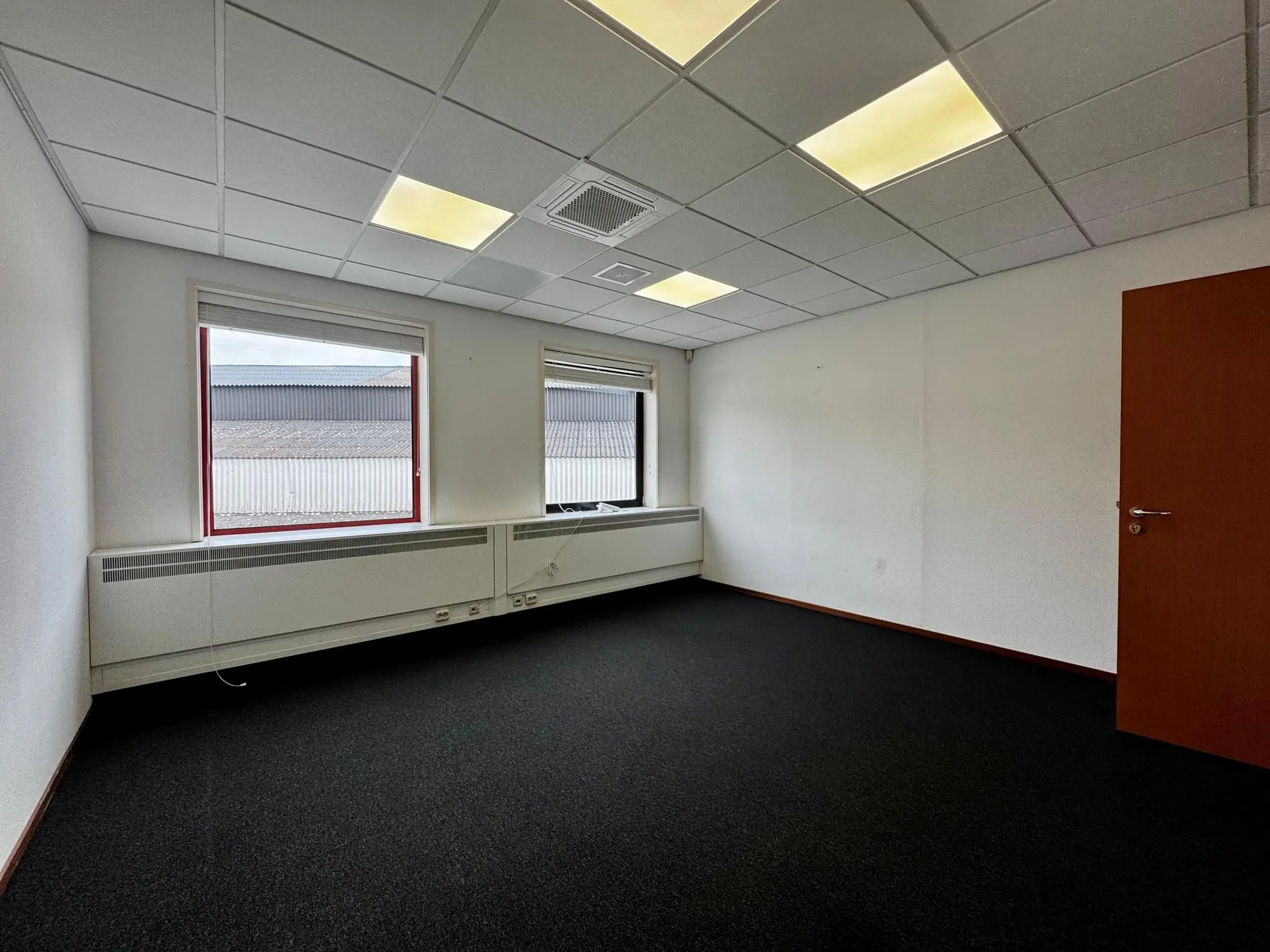 Leeg kantoorruimte met systeemplafond, twee ramen en een houten deur aan de Kwekerijweg.