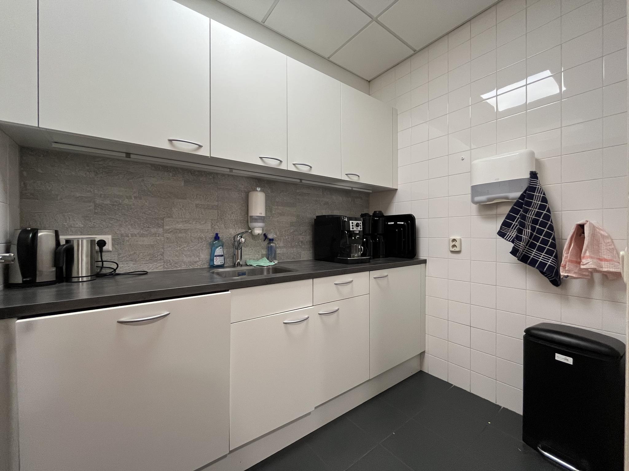 Moderne bedrijfskeuken aan de Kwekerijweg met witte kastjes, een koffiezetapparaat en diverse keukenapparaten.