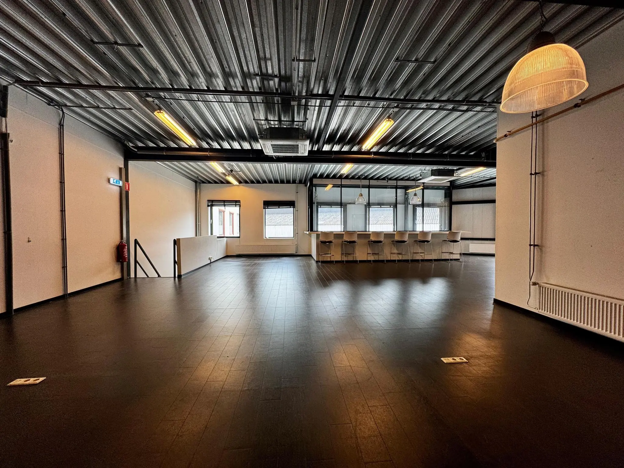 Ruime, industriële kantoorruimte aan de Kwekerijweg met donkere vloer, metalen plafond en een moderne keuken met barkrukken.