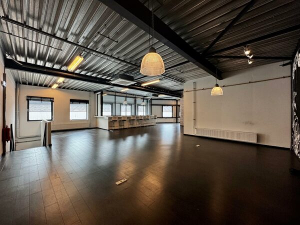 Ruime, industriële kantoorruimte aan de Kwekerijweg met donkere vloer, grote ramen en een bar met barkrukken.