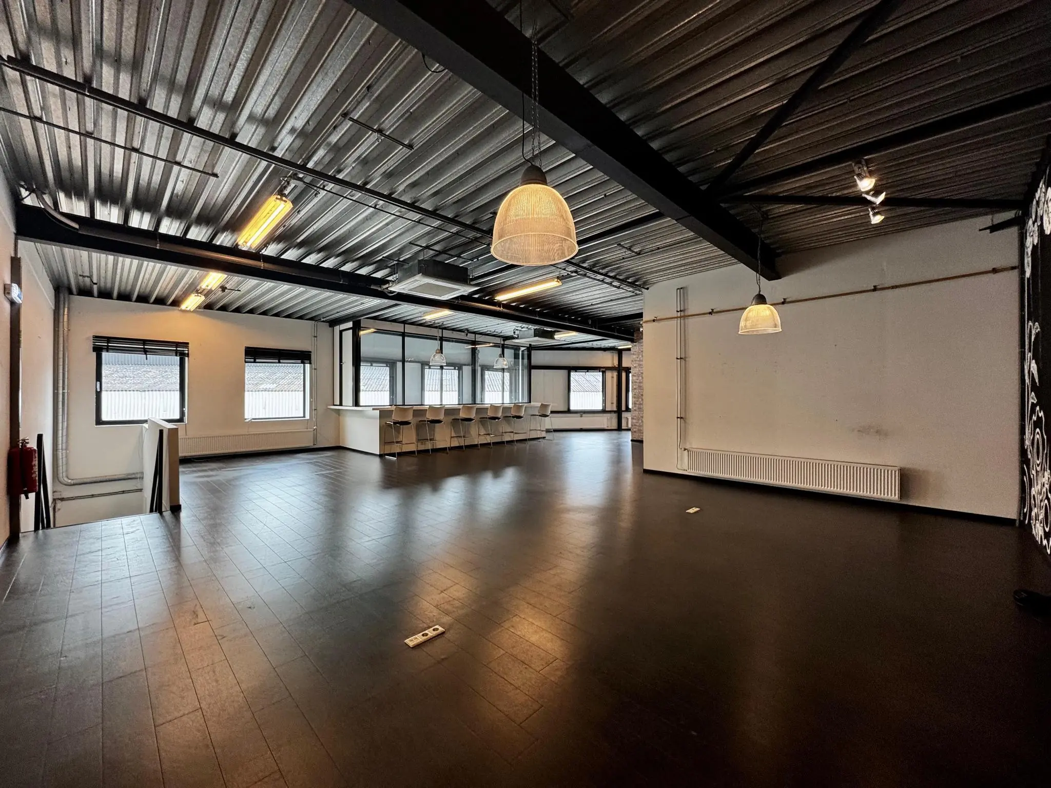 Ruime, industriële kantoorruimte aan de Kwekerijweg met donkere vloer, grote ramen en een bar met barkrukken.