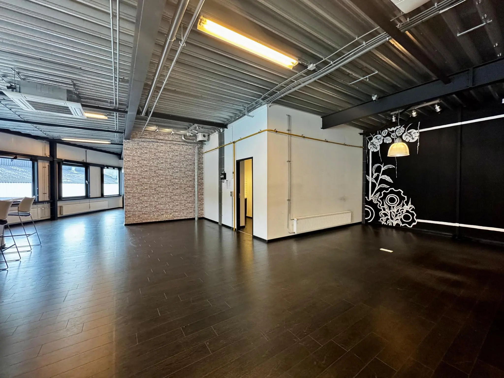 Moderne, lege kantoorruimte aan de Kwekerijweg met donkere vloer, industriële plafonds en een muurschildering met bloemen.