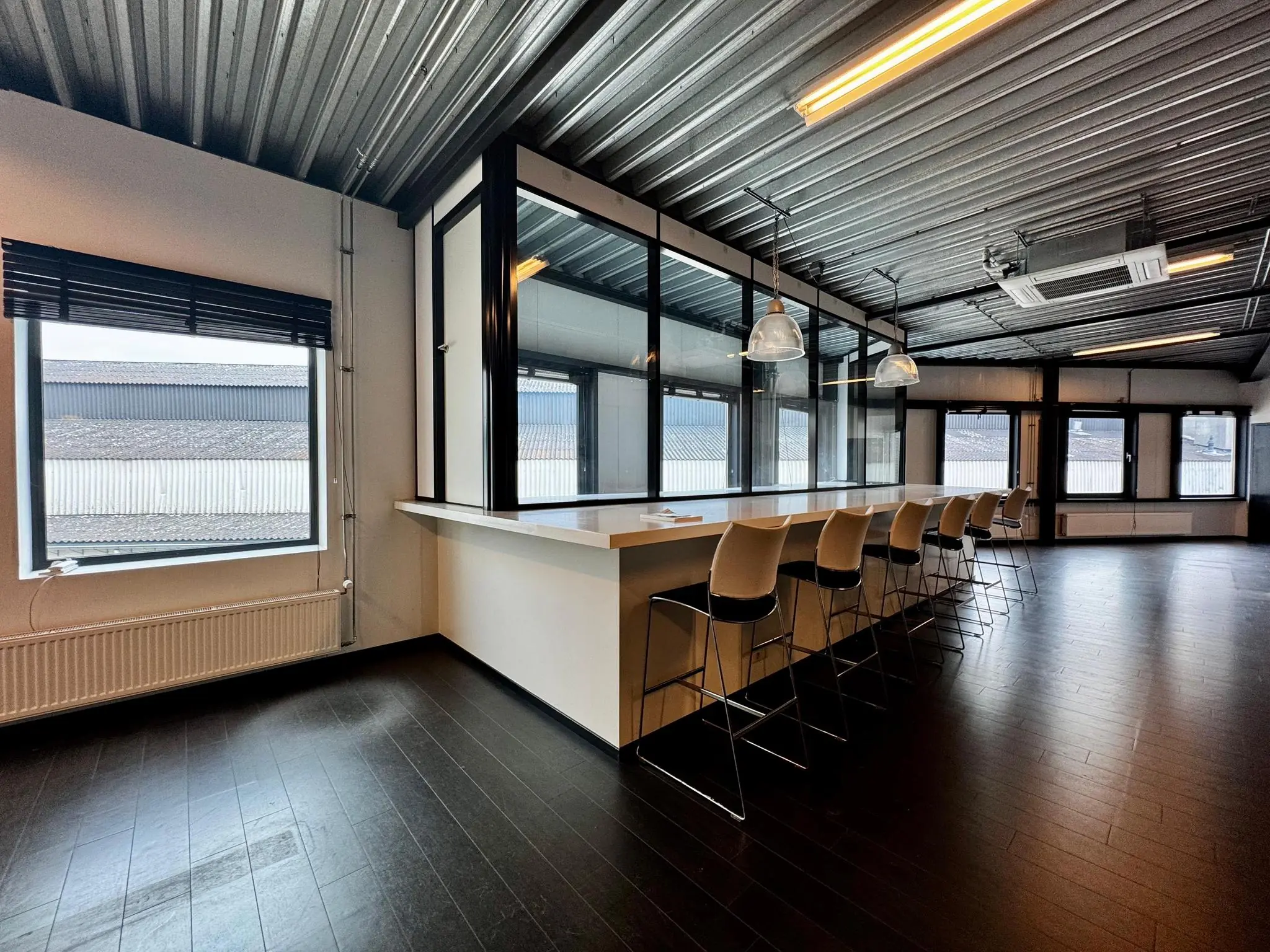 Moderne kantoorruimte aan de Kwekerijweg met hoge plafonds, grote ramen en een lange bar met barkrukken.