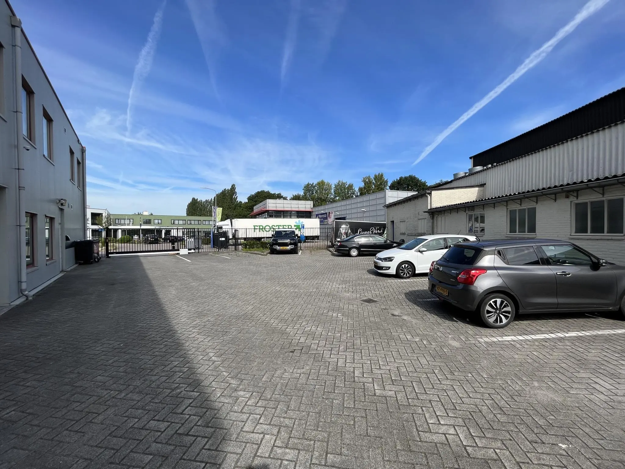 Bedrijventerrein aan de Kwekerijweg met geparkeerde auto's en bedrijfsgebouwen onder een blauwe lucht.