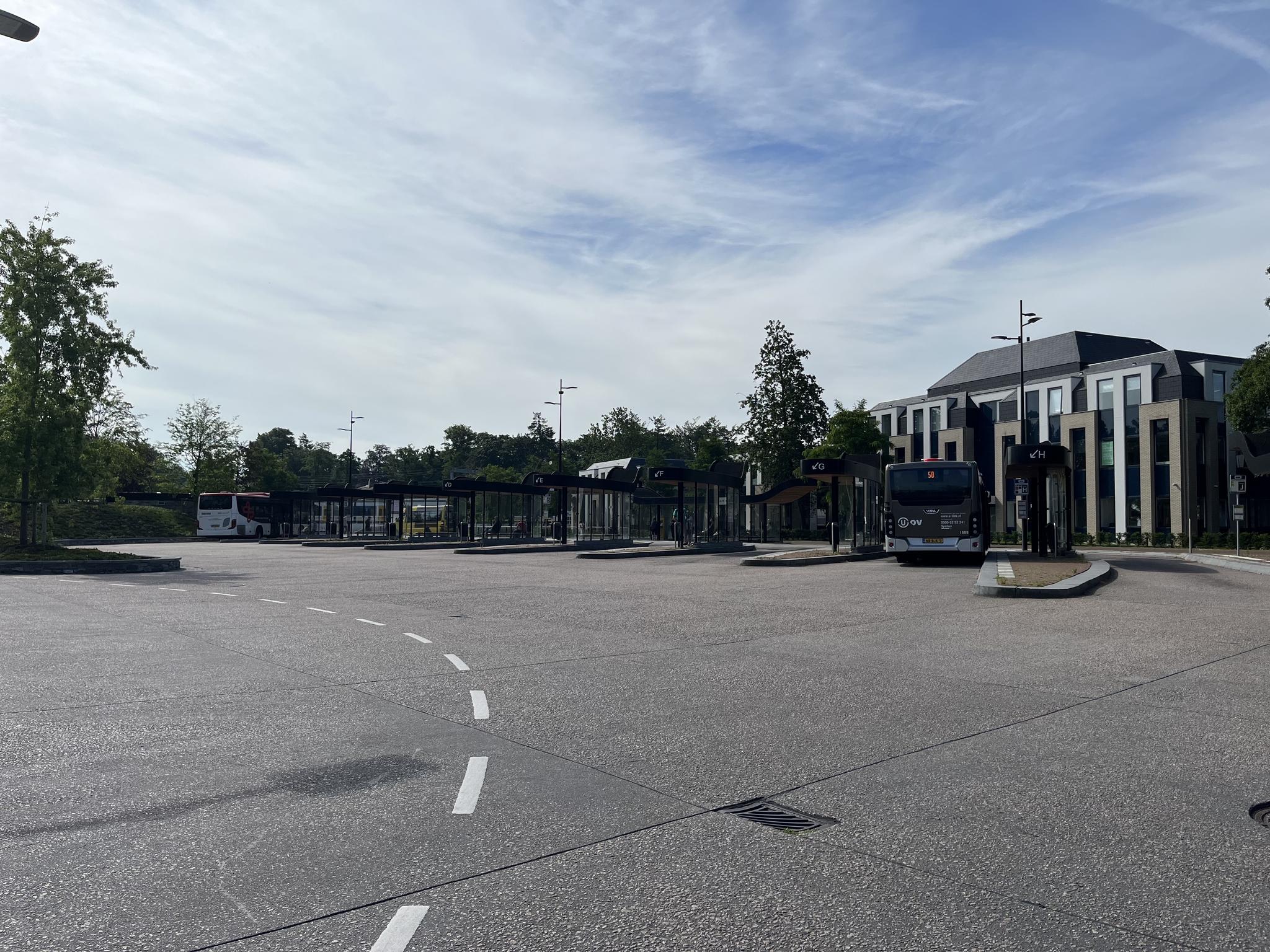 Busstation aan de Kwekerijweg met meerdere bussen en wachthokjes op een rustige ochtend.