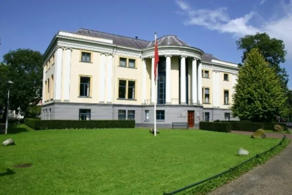 Klassiek gebouw aan de Museumlaan met zuilen en een vlag op een goed onderhouden grasveld.